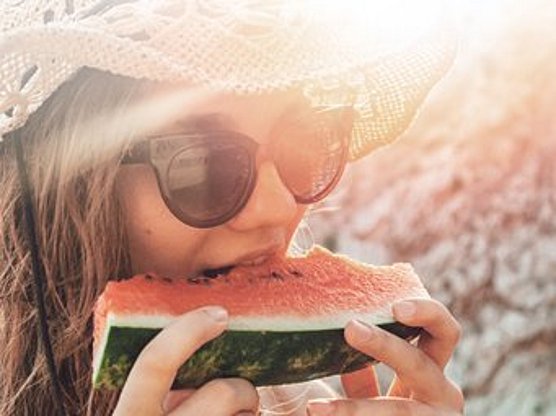 Eine Person mit Sonnenhut und Sonnenbrille isst im Freien ein Stück Wassermelone. Der Text auf dem Bild enthält Informationen, Therapie und Tipps zu Kreuzallergien. Der Hintergrund ist sonnig und leicht unscharf.